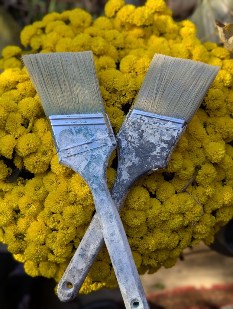Paint brushes crossed over yellow flowers